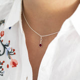 Mother and child birthstone necklace. A sterling silver chain pendant with a smaller birthstone in April Crystal and the larger stone representing mother in January red garnet. Model wears a white top.