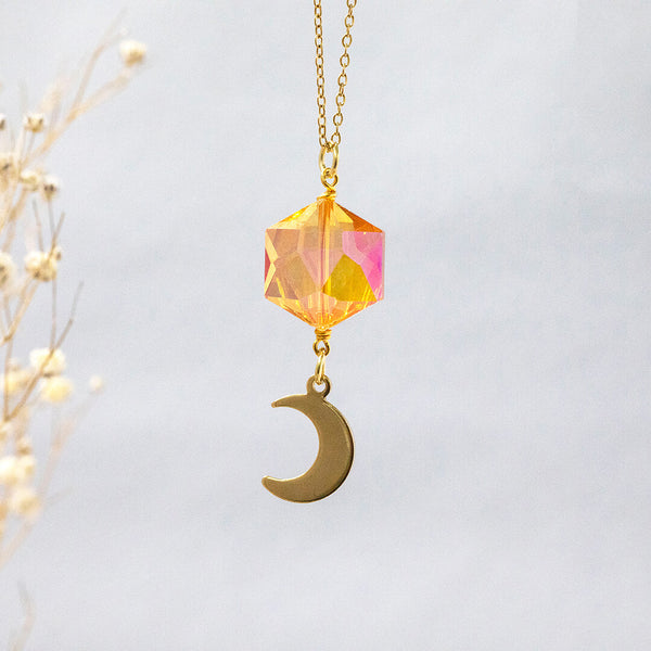 Image shows Oberon gold plated necklace with crescent moon charm suspended in front of a grey backdrop.