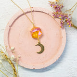 Image shows Oberon gold plated necklace with crescent moon charm on a pink and white backdrop.