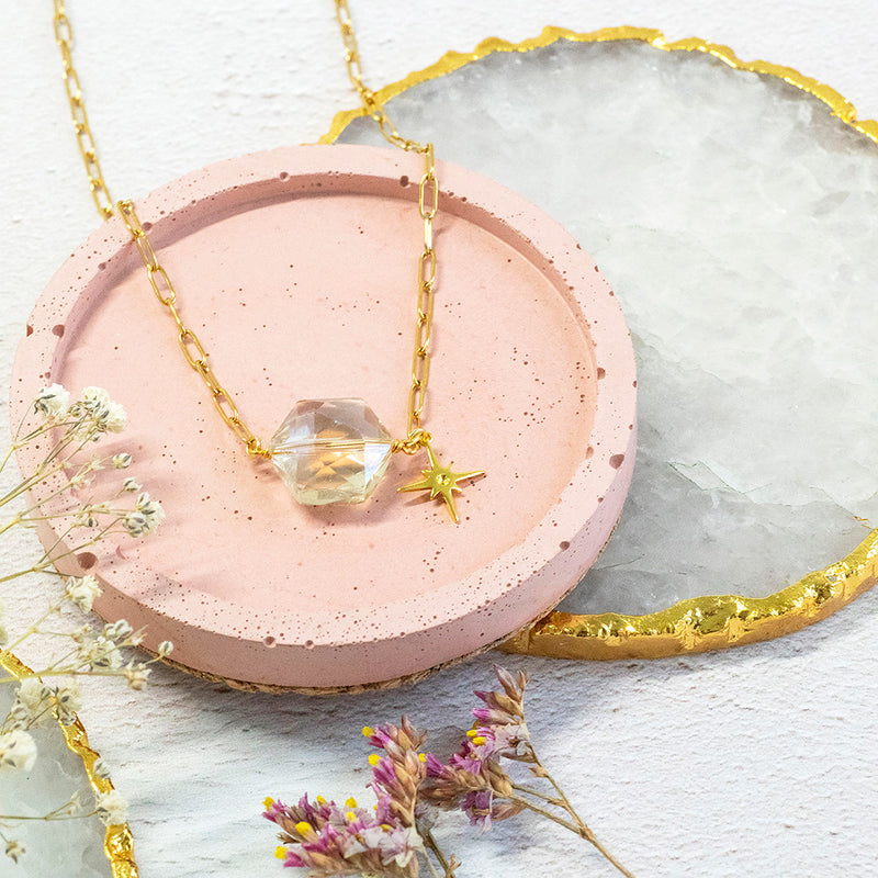 Image shows polaris gold plated necklace with star charm detail on a gorgeous gold link chain. Necklace sits on a pink backdrop. Matching bracelet available.