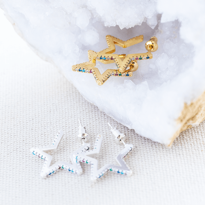 Image shows rainbow encrusted star shaped huggies, top pair is gold plated bottom pair is silver plated. Both encrusted with random multi coloured crystals. Earrings are on a white backdrop.