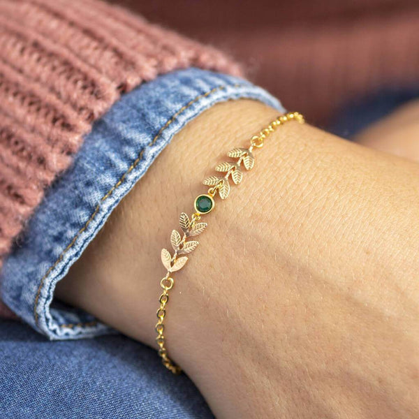 Model wears gold leaf vine bracelet with May emerald birthstone detail.