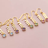 Image shows four pairs of gold leaf vine earrings on a pink backdrop. From left to right the Swarovski birthstones displayed are March aquamarine, February amethyst, August peridot and October rose.