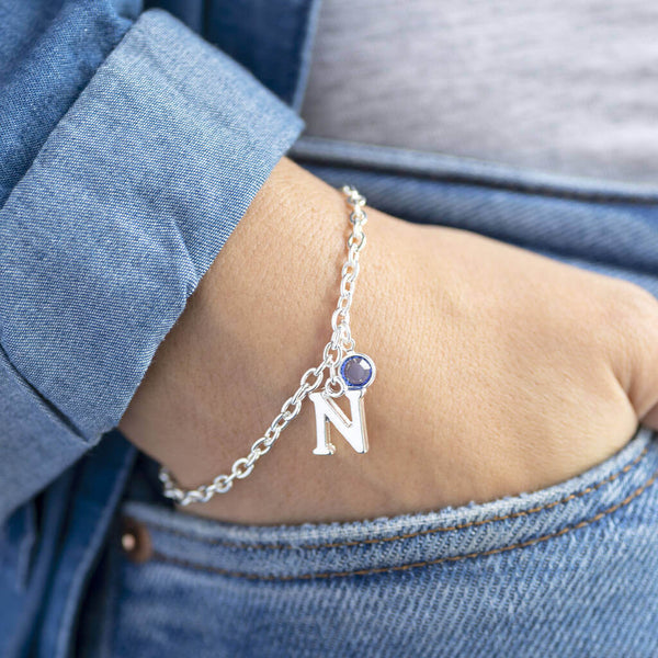 Model wears silver plated initial and charm bracelet, with the initial 'N' and the September Sapphire swarovski birthstone crystal.