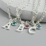 Image shows a collection of three silver plated initial and birthstone charm bracelets one a grey background. Bracelet displayed are the letter 'A' with a May Emerald Swarovski Crystal, the letter 'B' with an October Rose Swarovski Birthstone crystal and the letter 'C' with the March Aquamarine Swarovski birthstone.