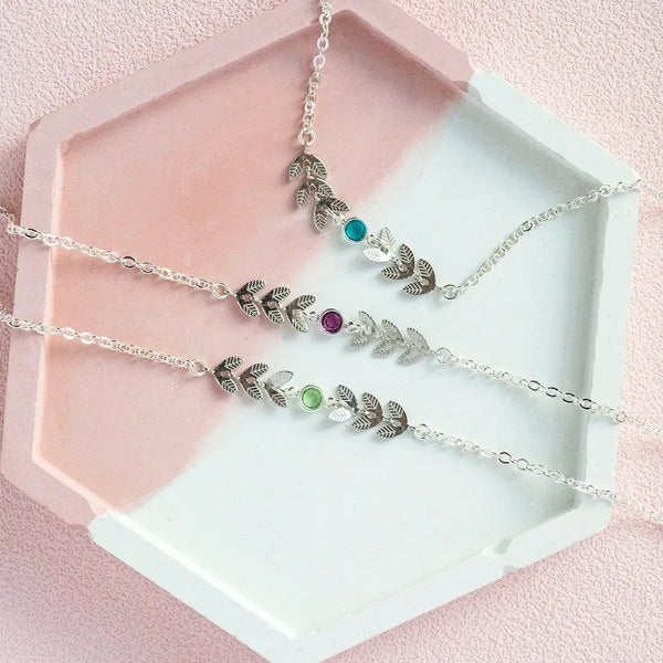 Image shows three delicate silver plated vine birthstone bracelets on a pink and white back drop. From top birthstones are: December blue zircon, February Amethyst and August Peridot.