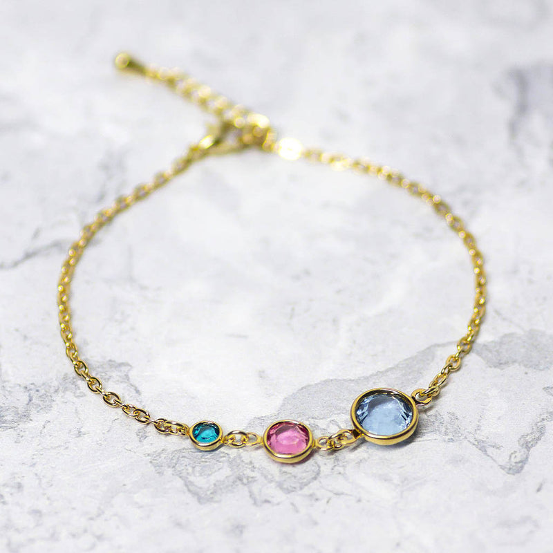 Image shows gold plated Three Generations Birthstone Bracelet with three birthstones. From left, December Blue Zircon, October Rose and March Aquamarine.