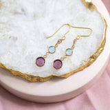 Gold plated Three Generations Birthstone Earrings. Birthstones in selection order from bottom to top: February Amethyst, March Aquamarine and October Rose. Earrings sit on a white crystal backdrop. 