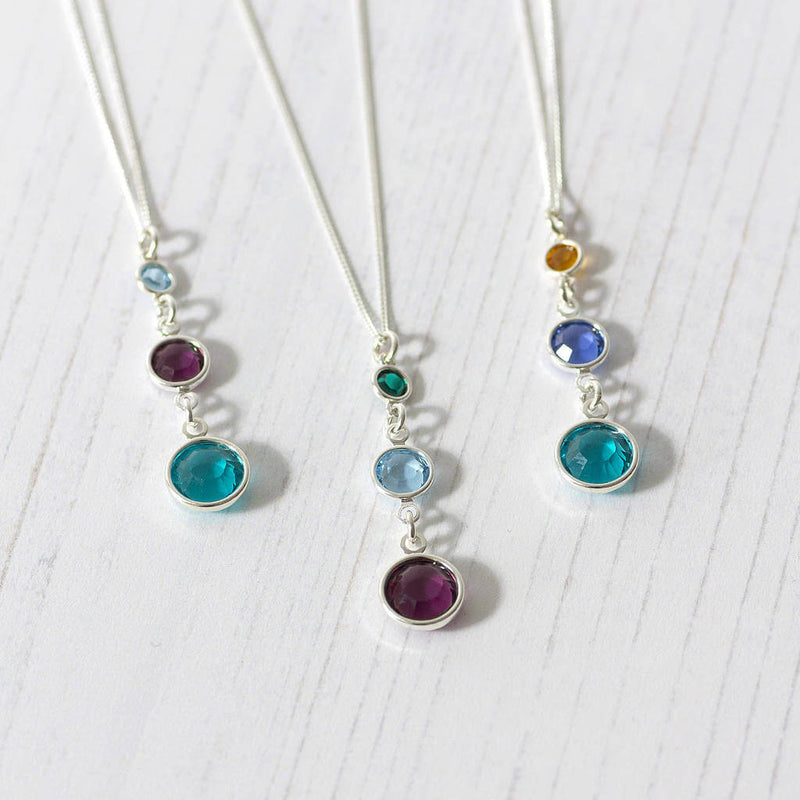 Image shows three different sterling silver Three Generations  Birthstone Necklaces. Necklaces form left to right. Necklace one, December Blue Zircon, February Amethyst and March Aquamarine. Necklace two, February Amethyst, March Aquamarine and December Blue Zircon. Necklace three has December Blue Zircon, September Sapphire and November Yellow Topaz on a white backdrop.