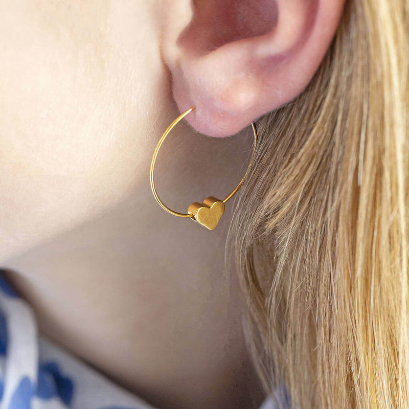 Model wears tiny gold plated heart hoop earrings in 6mm.