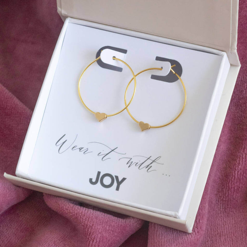 Image shows tiny gold plated heart hoop earrings in size 4mm, displayed on a 'Wear it with joy' sentiment card within the JOY branded giftbox.