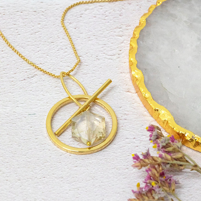 Image shows venus hexagonal necklace with a clear crystal hex within a golden circle pendant on a long length chain.