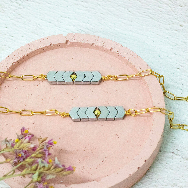 image shows two asteria hematite link gold plated bracelets on a pink circular backdrop.