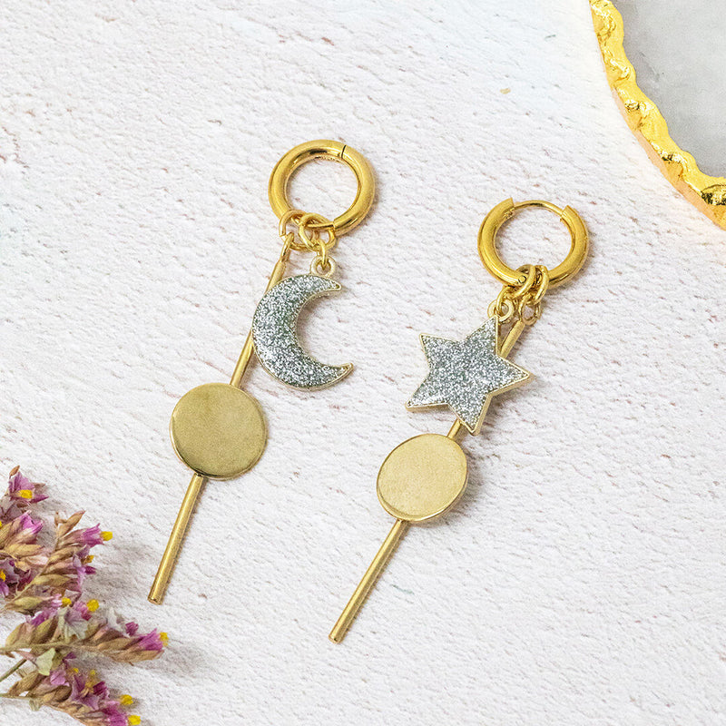 Image shows a pair of celeste moon and stars gold plated earrings. Left earring has rescent moon and right earring has a star.. Earrings on a white backdrop.