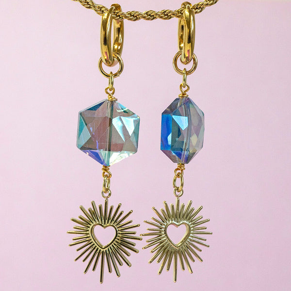 Image shows blue crystal cosmic heart earrings in front of a pink backdrop