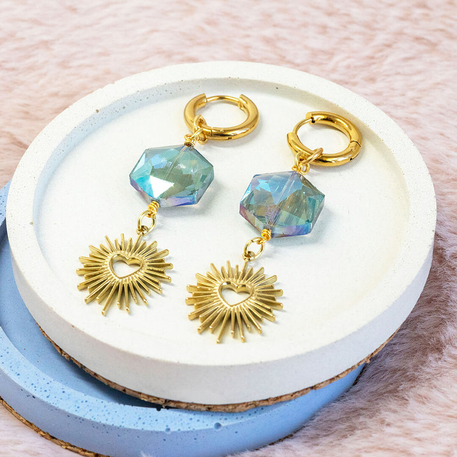 Image shows blue crystal cosmic heart earrings on a white backdrop