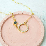 image shows crystal moon gold plated necklace with black star charm detail on a pink background.