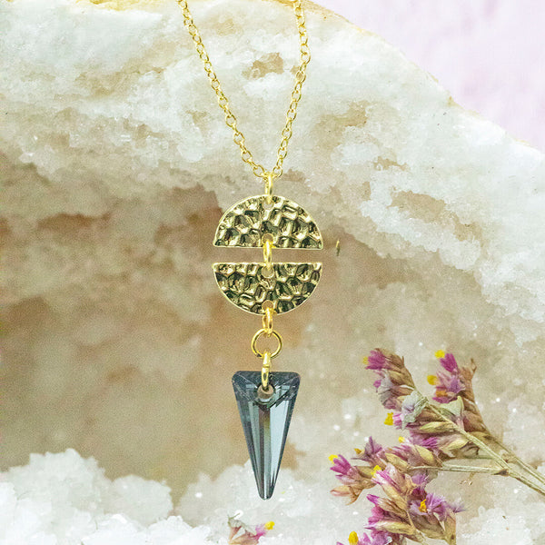 Image shows Ero Black crystal gold plated necklace in front of a white crystal backdrop.