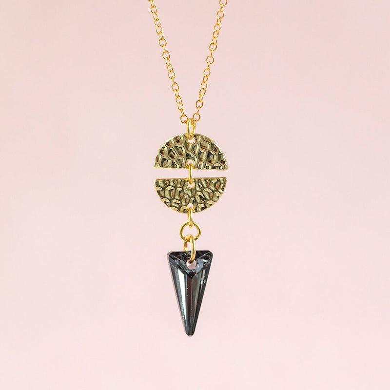 Image shows Ero Black crystal gold plated necklace on a pink backdrop.