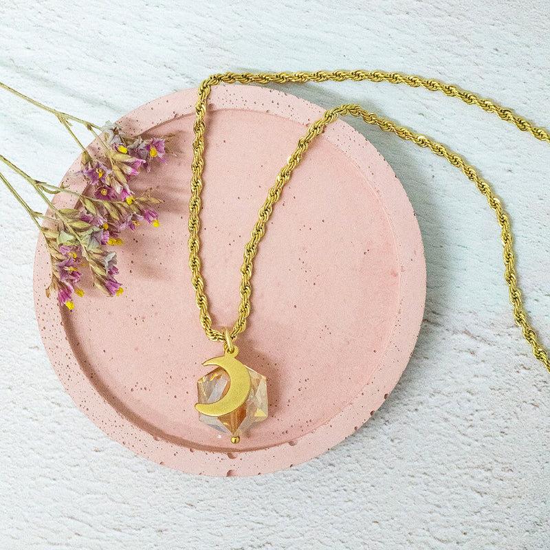 Image shows golden hexagon crystal and golden moon pendant on a pink circular backdrop.