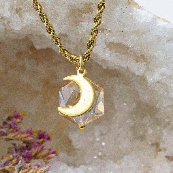 Image shows golden hexagon crystal and golden moon pendant with a crystal backdrop.