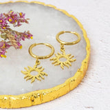 Helios gold plated earrings with sunburst on a crystal white backdrop.