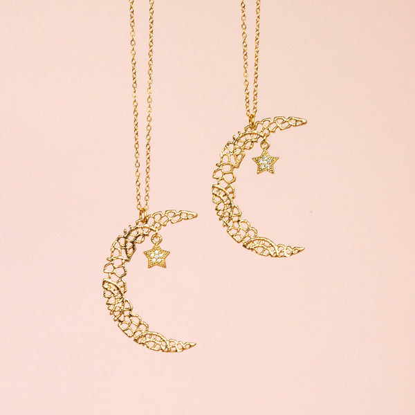 Image shows two Nova crescent moon pendant necklaces suspended in front of a pink background