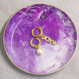 image shows gold hoop earrings with joy and pearl charms on a purple trinket dish.