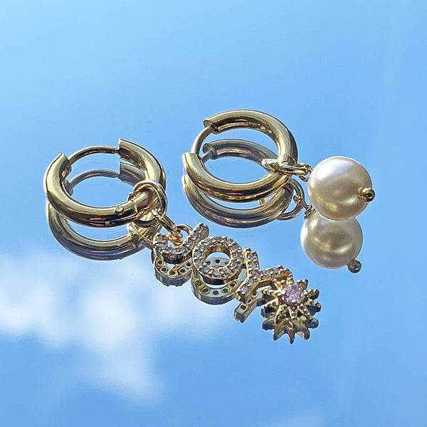 image shows gold hoop earrings with joy and pearl charms on a blue sky background