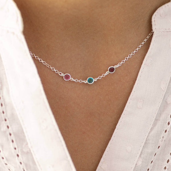 Model wears sterling silver mini birthstone link necklace with three Swarovski birthstones. From left to right birthstones are: October Rose, December Blue Zircon and February Amethyst.