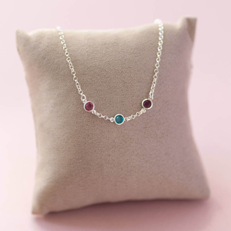 Image shows sterling silver mini birthstone link necklace with three Swarovski birthstones on a jewellery pillow. From left to right birthstones are: October Rose, December Blue Zircon and February Amethyst.