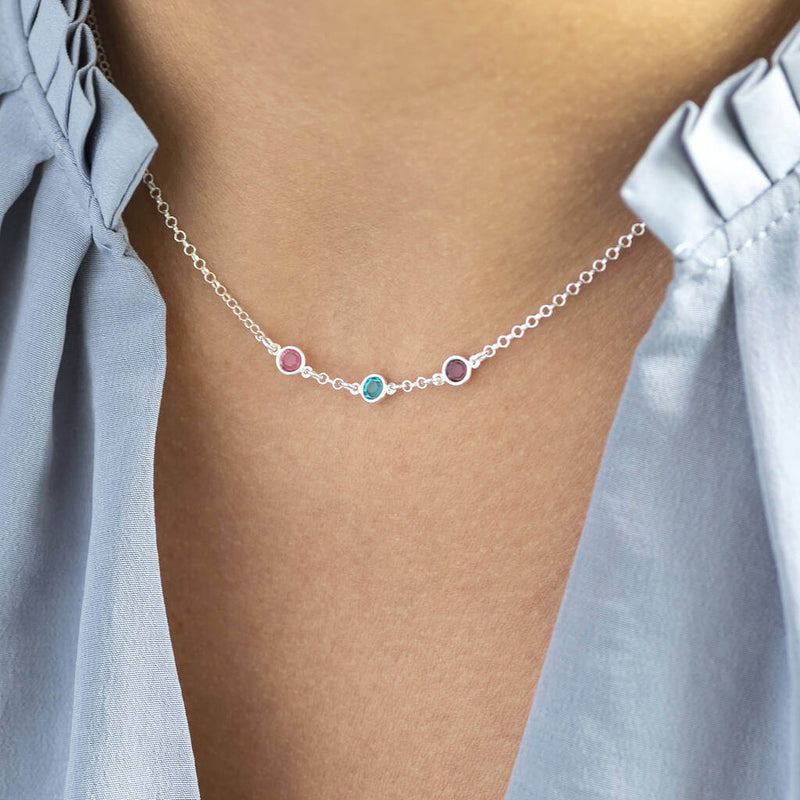 Model wears sterling silver mini birthstone link necklace with three Swarovski birthstones. From left to right birthstones are: October Rose, December Blue Zircon and February Amethyst.