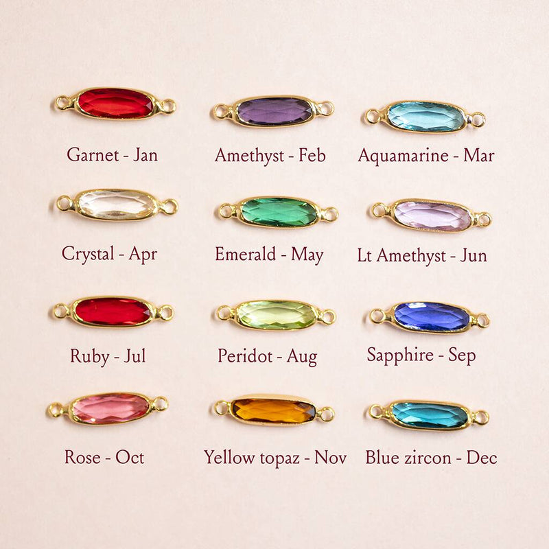 Images shows oval shaped crystal birthstones available from top left; Garnet January, Amethyst February, Aquamarine March, Crystal April, Emerald May, Light Amethyst June, Ruby July, Peridot August, Sapphire September, Rose October, Yellow Topaz November, Blue Zircon December.