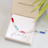 image shows one gold plated and one silver plated oval link family birthstone bracelet on a 'family' sentiment card and JOY by corrine smith gift box.