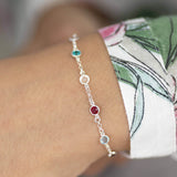 Model wears Sterling silver mini family birthstone bracelet with six birthstones (up to eight can be selected) from left to right birthstones are October Rose, May Emerald, April Crystal, July Ruby, March Aquamarine and February Amethyst.