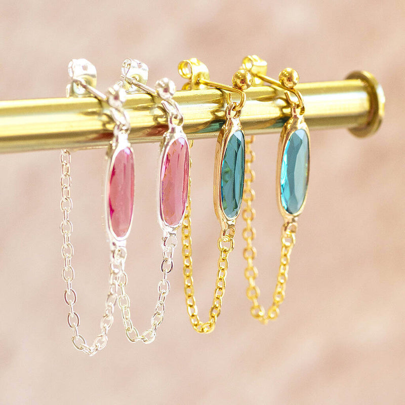 image shows two pairs of oval birthstone chain drop earrings, left set in silver and right set in gold plated with october rose and december zircon birthstones.