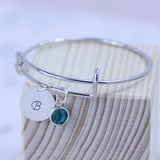 Image shows personalised birthstone christening bangle with Swarovski birthstone and hand stamped initial disc with the letter 'B'