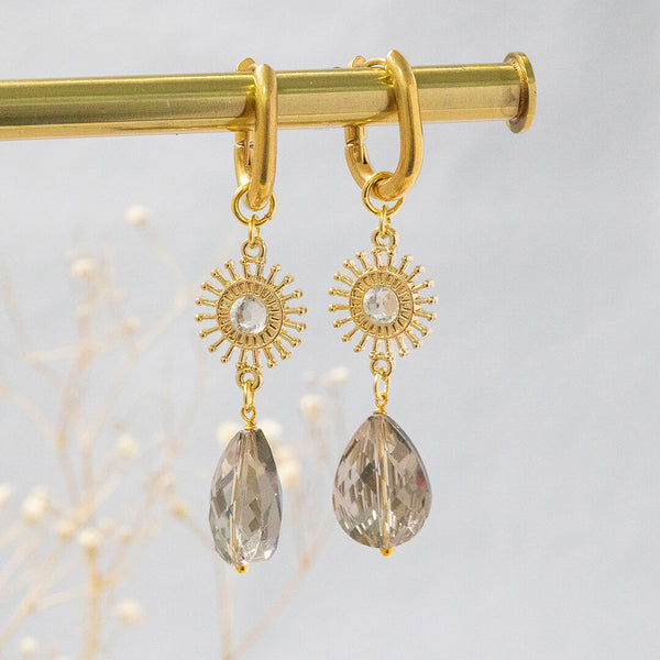 image shows radiance sunburst earrings with grey crystal and sunburst charm on a grey background.