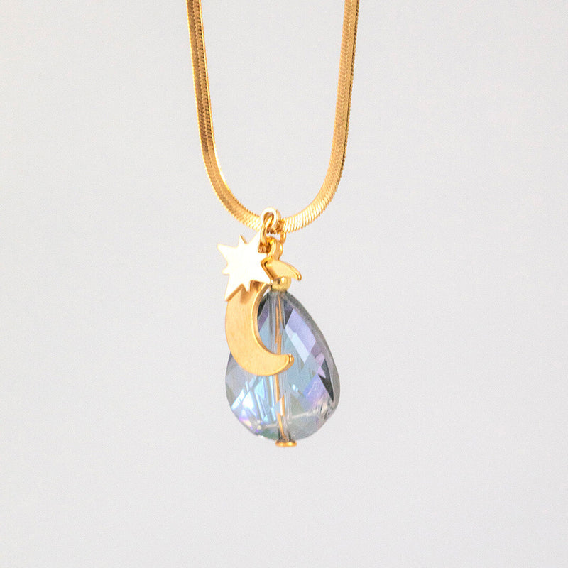 Image shows selene moon and star gold plated pendant with blue teardrop crystal. On a grey background.