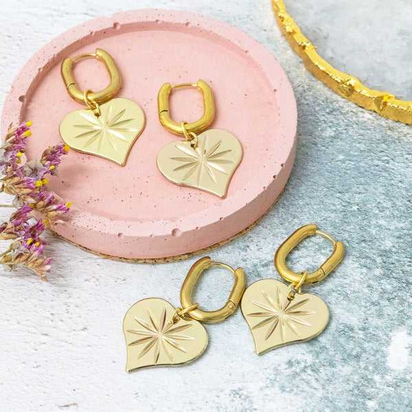 Starstruck gold plated heart earrings son a pink and white backdrop.