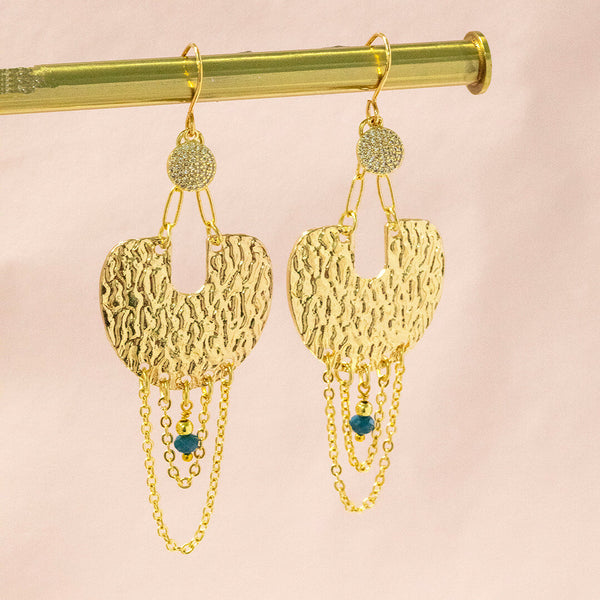 Image shows vega statement earrings with golden pave full moon, complete with chains and an indigo bead. Suspended in front of a pink backdrop.